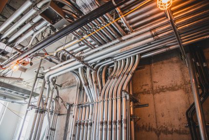 Professional installation of rigid metal electrical conduits in a commercial building, mounted on a concrete wall with construction lighting
