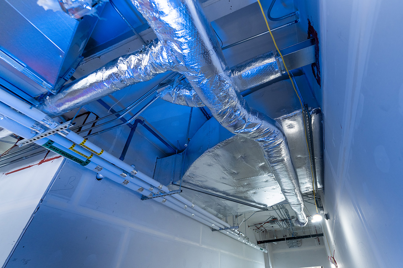 Ceiling of a commercial building under construction, with insulated reflective aluminum ventilation ducts suspended from a steel structure
