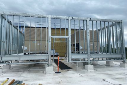 Mechanical equipment installation on a rooftop, with galvanized steel framing under construction and Daikin ventilation units in the background