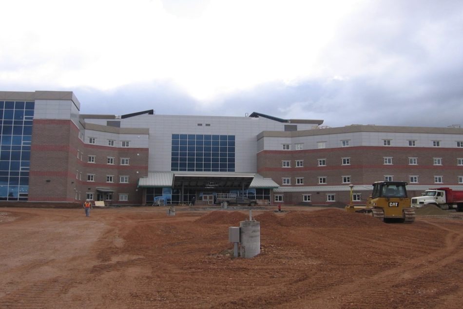 Hôpital en construction à Corner Brook avec machinerie lourde sur le chantier et façade moderne en briques et panneaux d’aluminium