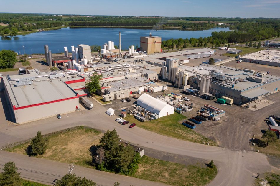 Vue aérienne de l’usine Parmalat à Victoriaville, avec bâtiments industriels, silos, équipements de production et un plan d’eau en arrière-plan
