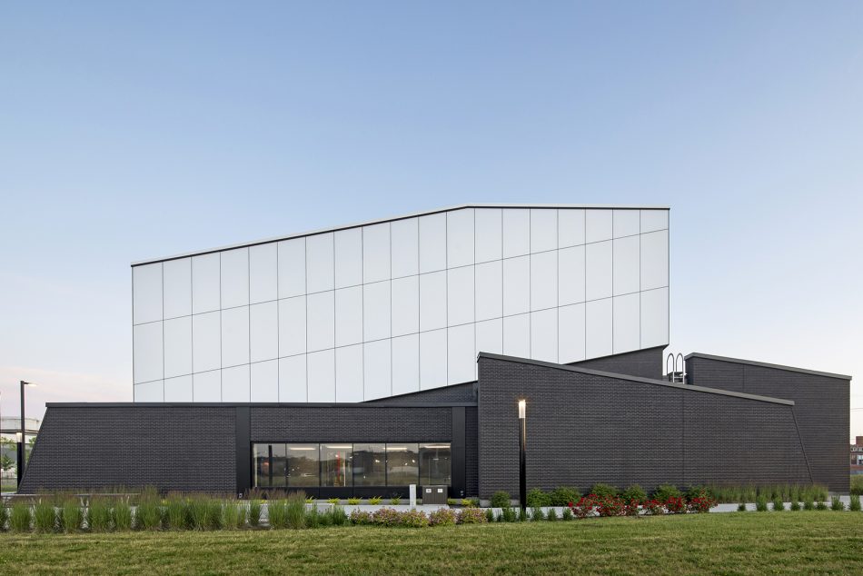 Vue extérieure de la station Côte-Vertu de la STM, montrant un bâtiment à l’architecture moderne avec façade noire texturée, volume supérieur blanc et aménagement paysager soigné