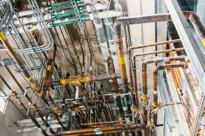 Complex mechanical piping installation on the ceiling of a hospital under construction at Santa Cabrini, including chilled water, heating, and medical gases
